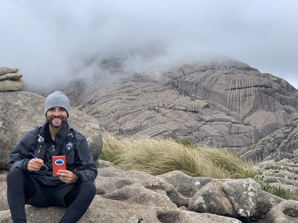 Summit log at Pedra do Sino, with Pico das Agulhas Negras in the background
